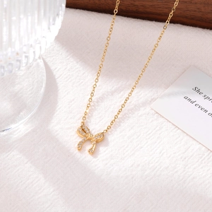 Elegant gold bow pendant necklace with sparkling rhinestones on a white textured background