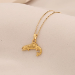 Minimalist golden fish pendant necklace with fine chain over beige fabric backdrop