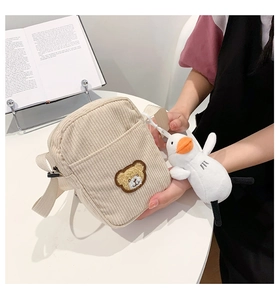 Detail of beige corduroy shoulder bag featuring bear embroidery and plush duck charm