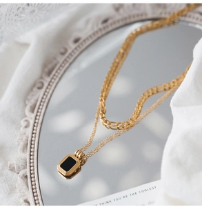 Macro detail of double-layer gold titanium necklace with black rectangle pendant on mirror