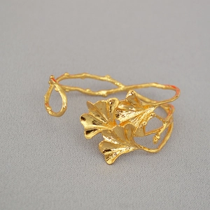 Gedetailleerd zicht op de geborstelde gouden ginkgobladtextuur op de open armband