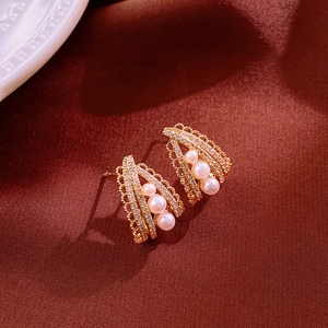Detail of vintage gold earrings with zircon pave and three vertical pearls on red silk