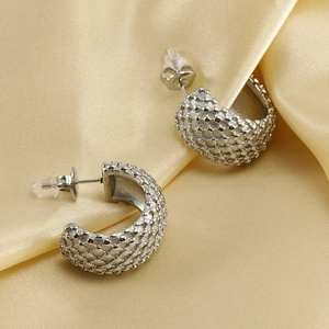 Macro shot of silver textured C-shape stud earrings on champagne satin background