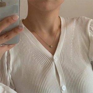Close-up of a gold micro-set zircon cylinder pendant necklace on a ribbed cardigan