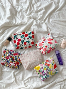 Flat lay of five vintage floral cotton makeup bags with zippers on white linen fabric