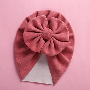 Close-up of soft coral pink knitted baby beanie featuring a large decorative bow