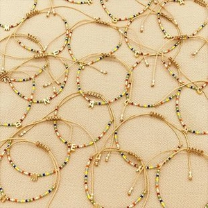 Macro view of handmade braided bracelets with gold alloy initial letter pendants and beads