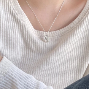 Macro view of 925 sterling silver necklace with oval flower pendant on white knitwear