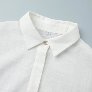 Vue macro détaillée du col de chemise en lin blanc avec bouton nacré et étiquette de taille S
