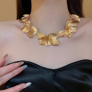 Detail of a large golden flower necklace with pleated texture on the petals shown on a model