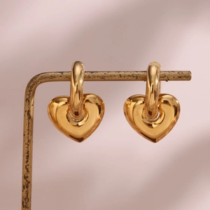 Detailed view of gold heart earrings hanging on a vintage metal stand in soft lighting