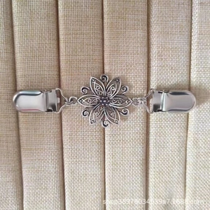 Détail d'un clip de gilet vintage argenté avec motif floral sur tissu beige