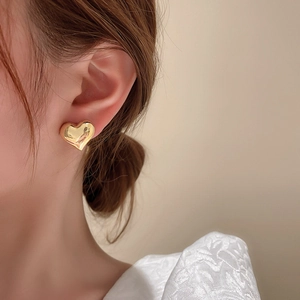 Detail shot of a model wearing elegant gold heart stud earrings with a metal finish