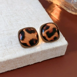 Close-up of square leopard print earrings with faux leather texture on a linen surface
