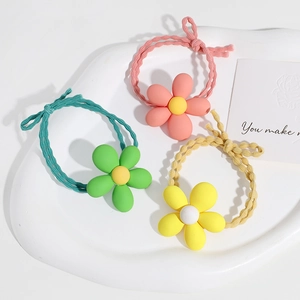 Three colorful floral elastic hair ties in pink, green, and yellow on a white ceramic tray