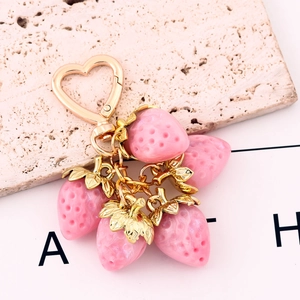 Macro shot of realistic pink strawberry keychain with heart-shaped golden clasp and leaves