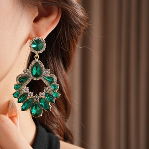 Gros plan de boucles d'oreilles dorées avec glands en cristal vert goutte d'eau sur modèle