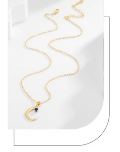 Detail of gold crescent moon necklace featuring a sapphire-blue stone and lobster clasp