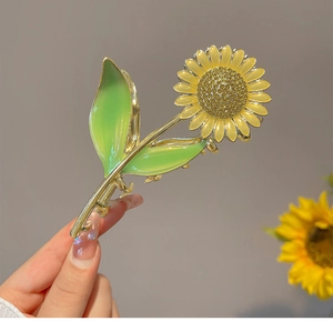 Detail of yellow enamel sunflower hair claw clip with golden metal and green leaves
