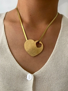 Close-up of gold hollow heart pendant on flat snake chain worn by a female model