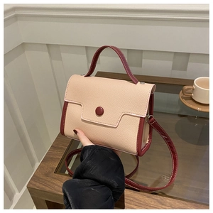Detail of beige litchi grain leather handbag with dark red trim and round clasp accent