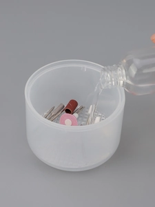 Action shot of liquid pouring into an nail tool sterilizer cup with various drill bits