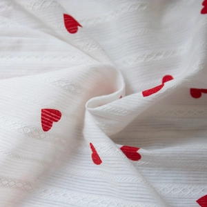 Détail du tissu en coton blanc avec motifs de cœurs rouges et broderie en dentelle fine