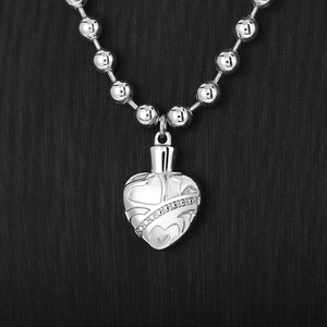 Close-up of silver steel beaded chain necklace with embossed heart pendant and crystal detail