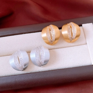Macro detail of C-shaped crisscross earrings in brushed gold and silver with zircon