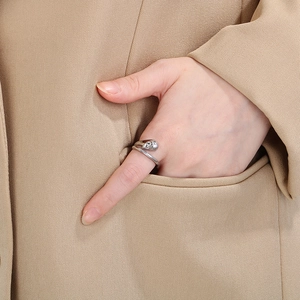 Close-up of a silver polished organic twisted ring on a finger with a beige coat backdrop