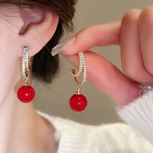 Close-up of red drop earrings with gold hooks and sparkling crystals on female ear