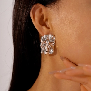 Close-up detail of silver wrinkled square stud earrings on female ear with metallic texture