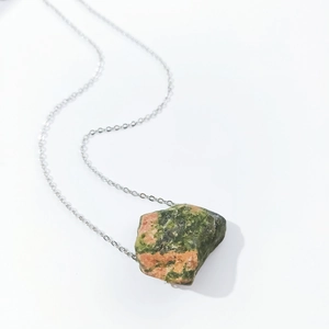 Macro shot of irregular natural green and orange crystal stone pendant on silver chain
