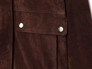 Detailed close-up of dark brown suede bomber jacket pocket with silver metal snap buttons