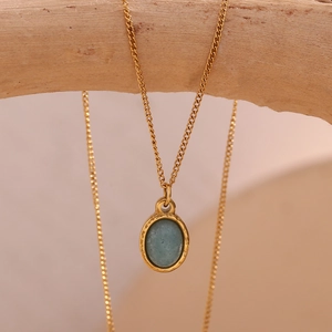 Detailed close-up of a 18K gold plated necklace with oval blue stone on a wooden branch