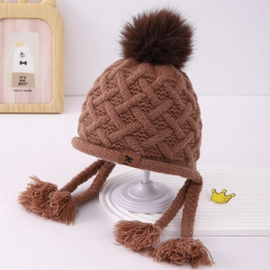 Detailed close-up of dark brown knit hat with cable texture and fluffy pom-pom