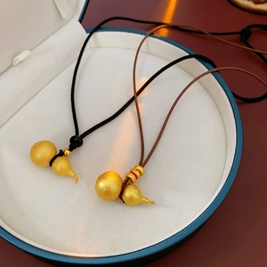 Detail view of gold-brushed gourd necklaces with black and brown braided cords in a gift box