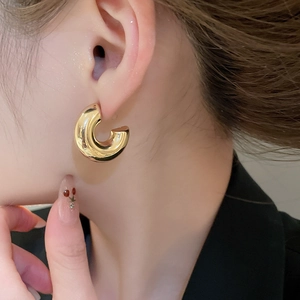 Close-up of chunky gold C-shaped hoop earrings worn on a model with black blazer