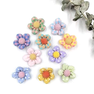 Flat lay of colorful fabric flower accessories with plaid and polka dot patterns on white
