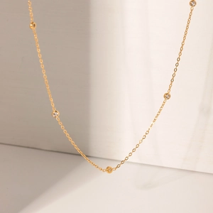 Detail shot of a minimalist gold necklace with bezel-set clear stones and delicate chain