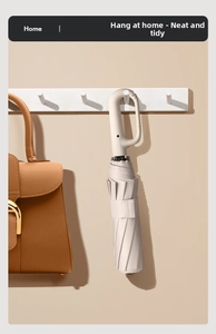 Detail of beige folding umbrella with carabiner handle hanging on a home wall hook