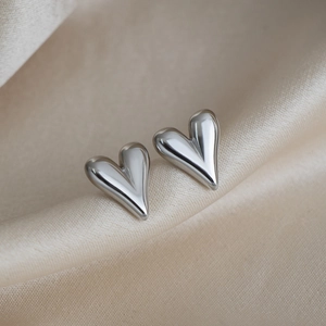 Macro shot of polished silver heart-shaped stud earrings on champagne silk fabric