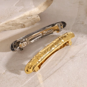 Textured gold and silver stainless steel hair clips on a minimalist stone background