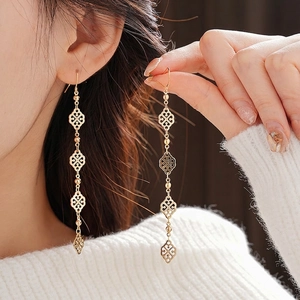 Elegant gold drop earrings with hollow geometric patterns worn on a white sweater background