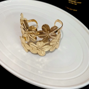 Detail of golden floral cuff bracelet showing brushed metal texture and 3D flower petals