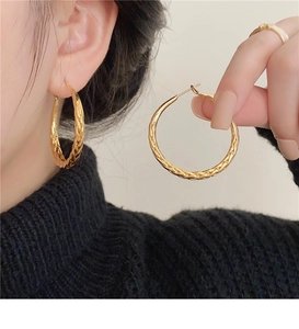 Macro shot of gold hoop earrings with twisted texture worn by model on beige backdrop