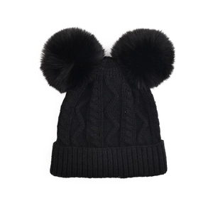 Détail d'un bonnet en maille torsadée noire avec deux pompons en fausse fourrure