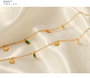 Close-up of gold geometric necklace with sun pendant and green zircon on cream satin