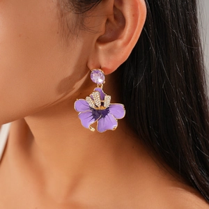 Detail of a floral drop earring with purple enamel petals and a crystal center on a model