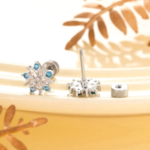 Silver snowflake earrings with blue and white zircon stones on a beige jewelry tray